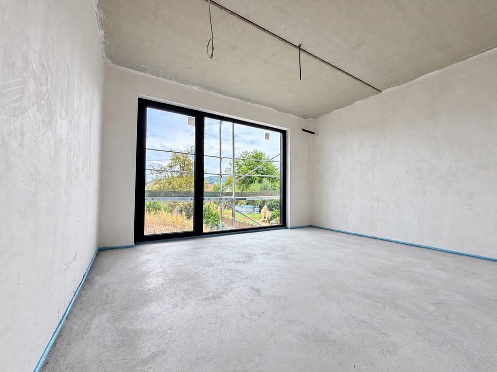 Rohbau-Innenraum mit fertigem Estrich und bodentiefem Fenster